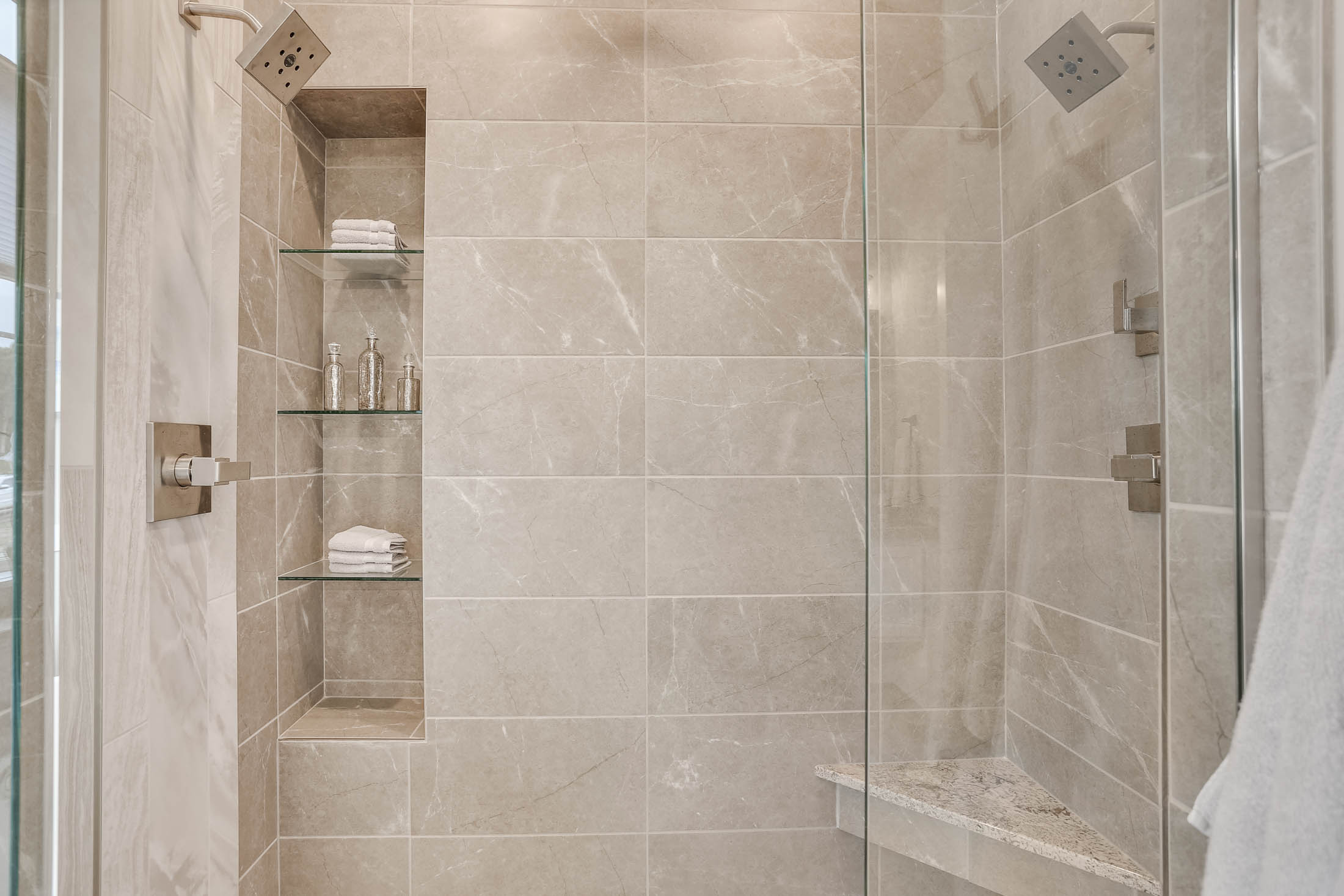 Glass door large tile shower with double shower heads and built-in niches